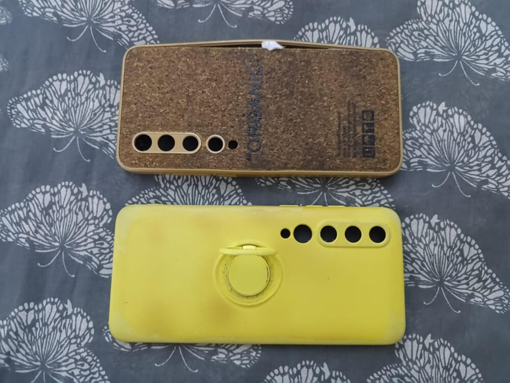 Cork case with the label "ORGANIC" and a yellow silicone case with a ring. Both show visible signs of aging, such as scratches and deformation.