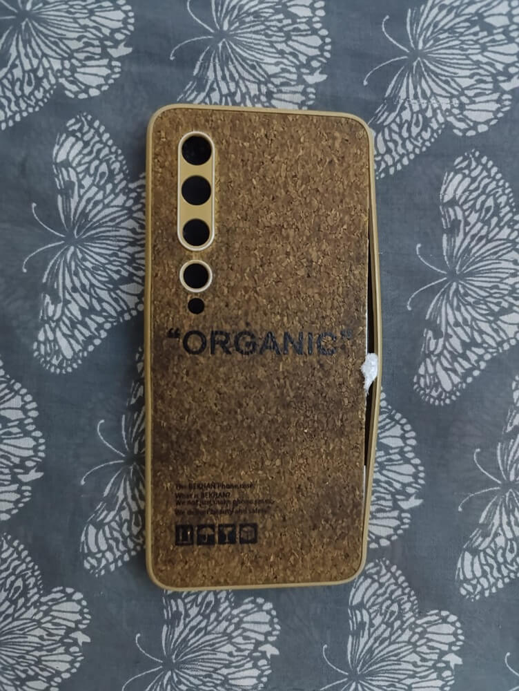 A close-up of a cork-textured phone case showing creases and slight damage on its surface. The background is a butterfly-patterned fabric.