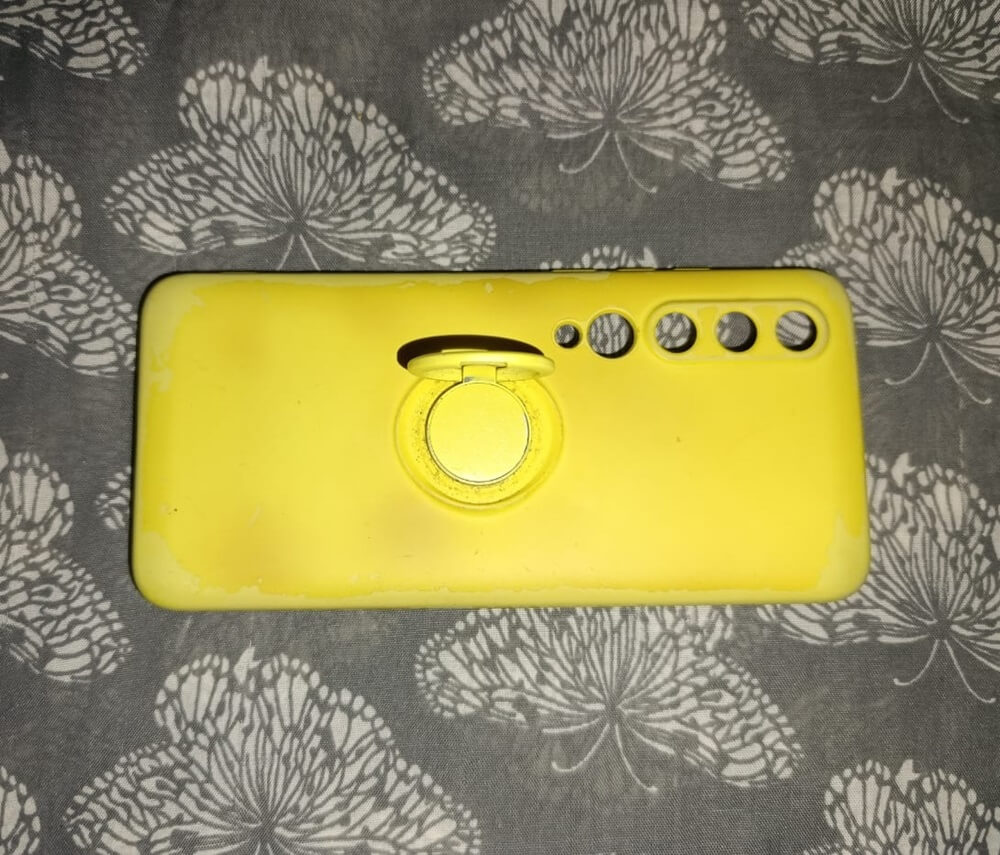 Yellow silicone case with ring stand exhibits scratches, discoloration, and visible damage from prolonged use.